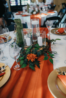 Table decor with candles, greenery, and orange flowers at Houston wedding reception.
