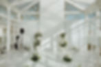 Greenhouse wedding setup with white florals, draped fabric, and clear chairs facing a floral arch