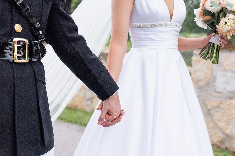 Close-up of bride and groom holding hands, bride in white gown holding bouquet.