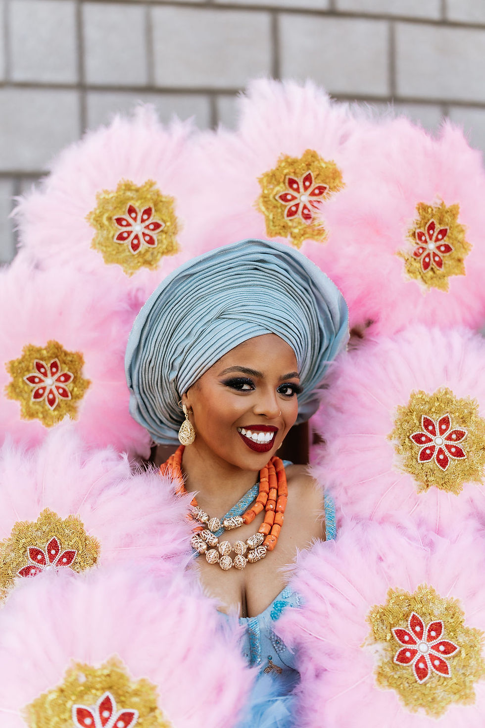 Bride's radiant smile in blue Nigerian wedding attire, framed by pink feathers