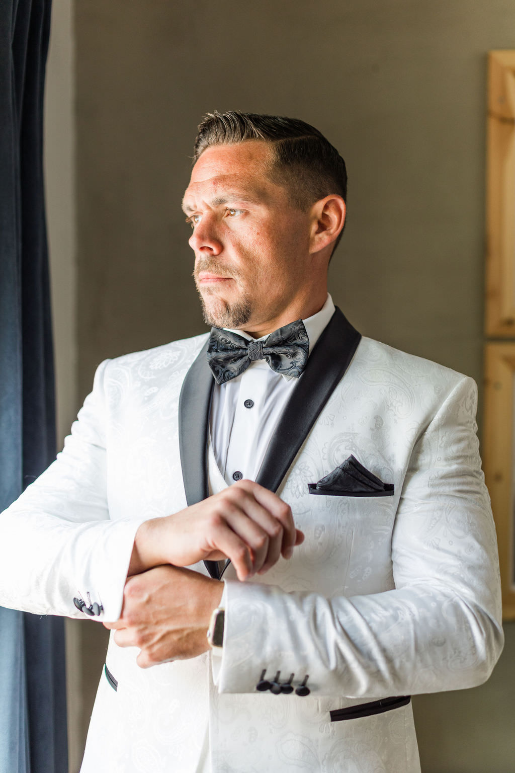 Groom in white tux getting ready before wedding ceremony.