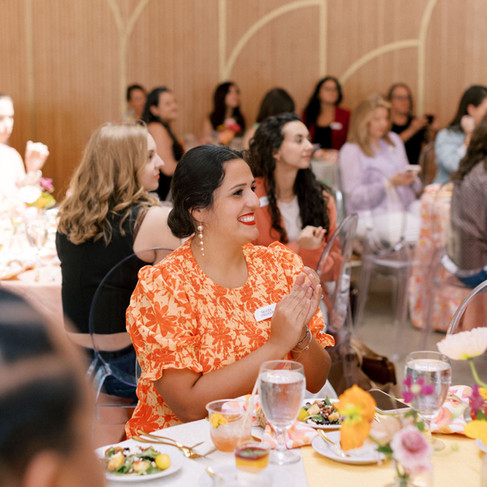 Brandi clapping during a wedding event surrounded by guests at decorated tables.