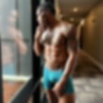 Shirtless Patrick Blackwood with tattoos looking out a window