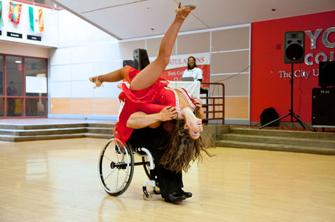 Nick Scott, a bodybuilder turned dancer in a wheelchair, skillfully flips his partner, Aubree Marchione, over his head during their dynamic performance at CUNY York University. Their synchronized movements display strength, agility, and artistic expression.