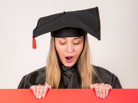 A female college student wearing a black graduation hat, looking down at a red poster she is holding