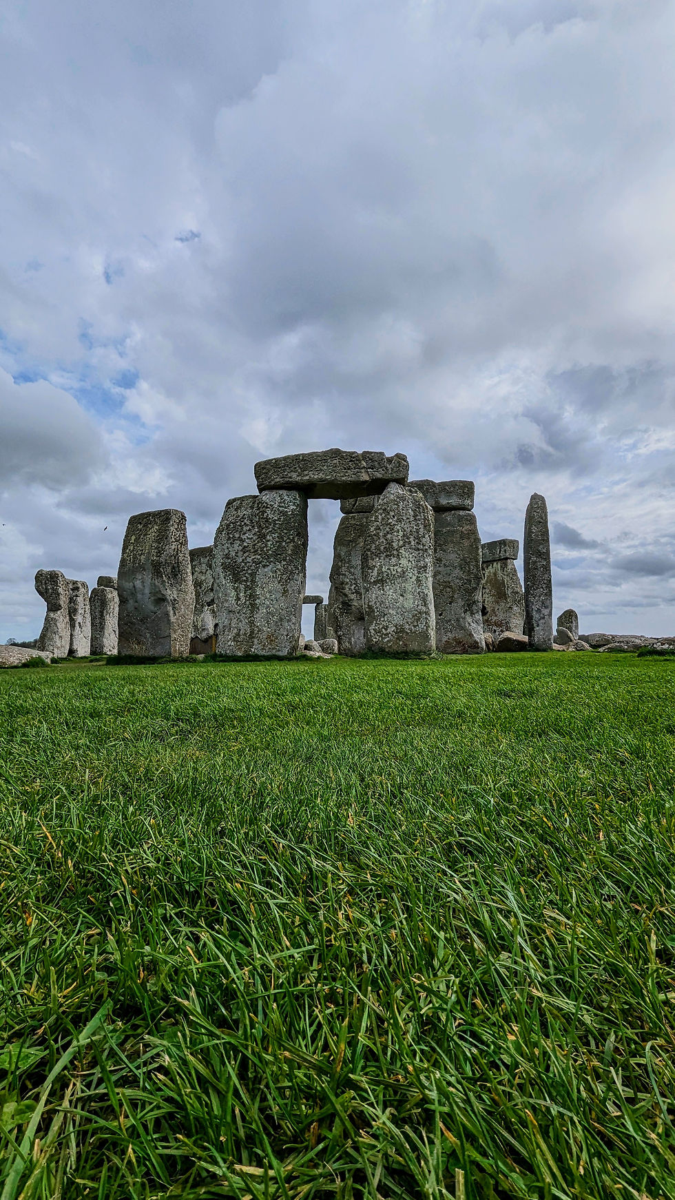 Stonehenge taken from a ground level angle. The grass is green and the backdrop is a cloudy sky