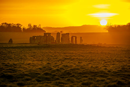 Stonehenge at sunrise, ancient stones against a golden sky, and a distant view.