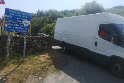 A white van parked in front of a blue sign that says 'Road suitable for cars and light goods vehicles only unsuitable for all vehicles in winter conditions' 
