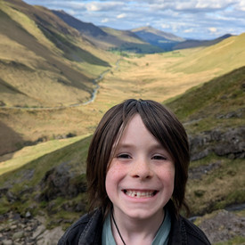 Theo standing in front of a mountain backdrop with green mountaind and a river 