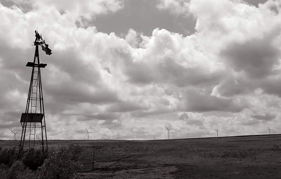 Black and white photo of an old water pump weather vane with modern wind turbines in the distance behind it