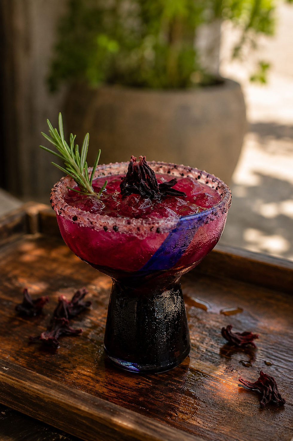 Hibiscus rosemary margarita with a hibiscus flower garnish, rosemary sprig, and chili-salt rim served in artisan Mexican glassware.