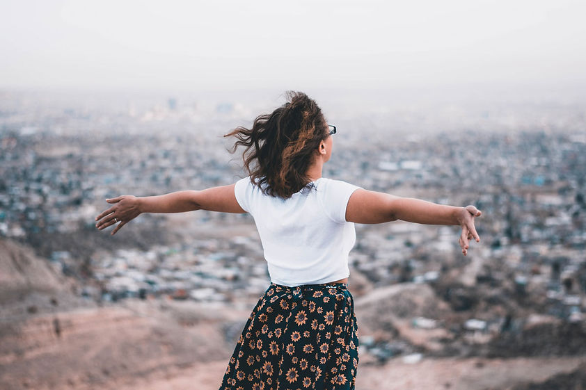 A healthcare professional stands with her arms out, facing away from the camera toward a beautiful view.