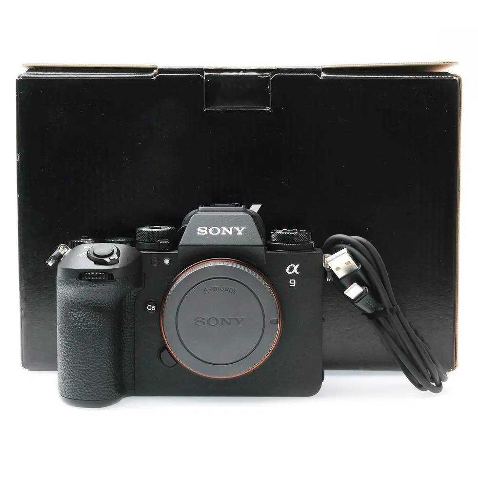 Black Sony a9 III camera with lens, charging cable, and box on white background.