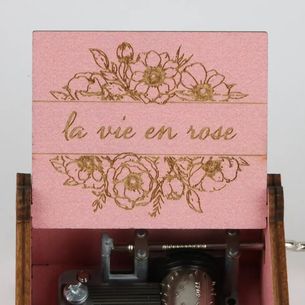 Miniatură: Close-up of personalized "La vie en rose" message and intricate floral design engraved inside a pink music box lid.