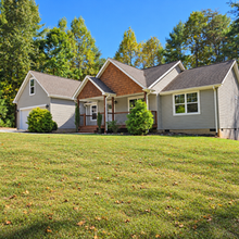 Front exterior of 15 Tiki Way with a wide lawn and wooded backdrop