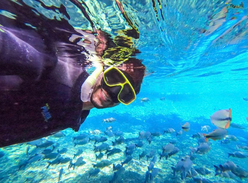 foto de homem tirando self dentro so rio olho d'agua enquanto mostra transparencia do rio e peixes