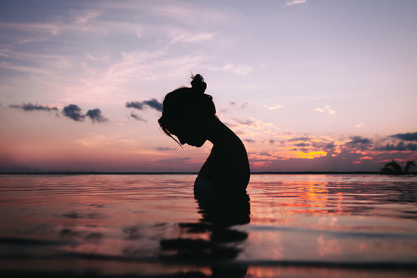 Silhouette of a woman rising out of ocean at sunset