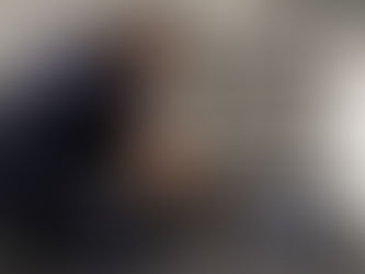 Man in donkerblauw Renz Jacobs Lekdetectie-uniform hurkt bij een open keukenkastje en gebruikt een akoestische lekdetector met koptelefoon om een leiding onder de gootsteen te controleren, met een Renz Jacobs Lekdetectie-koffer op de vloer ernaast.