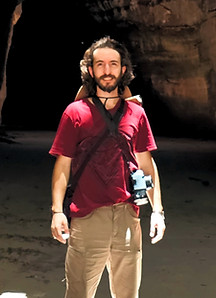 Foto de Fernando Vezzani olhando para a câmera, de pé, entre 2 paredões de cânions no sítio do João Pimenta