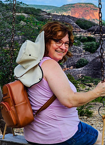 Foto da Claudia Vezzani em um balanço, sorrindo, enquanto ao fundo tem a paisagem do Sítio do João Pimenta