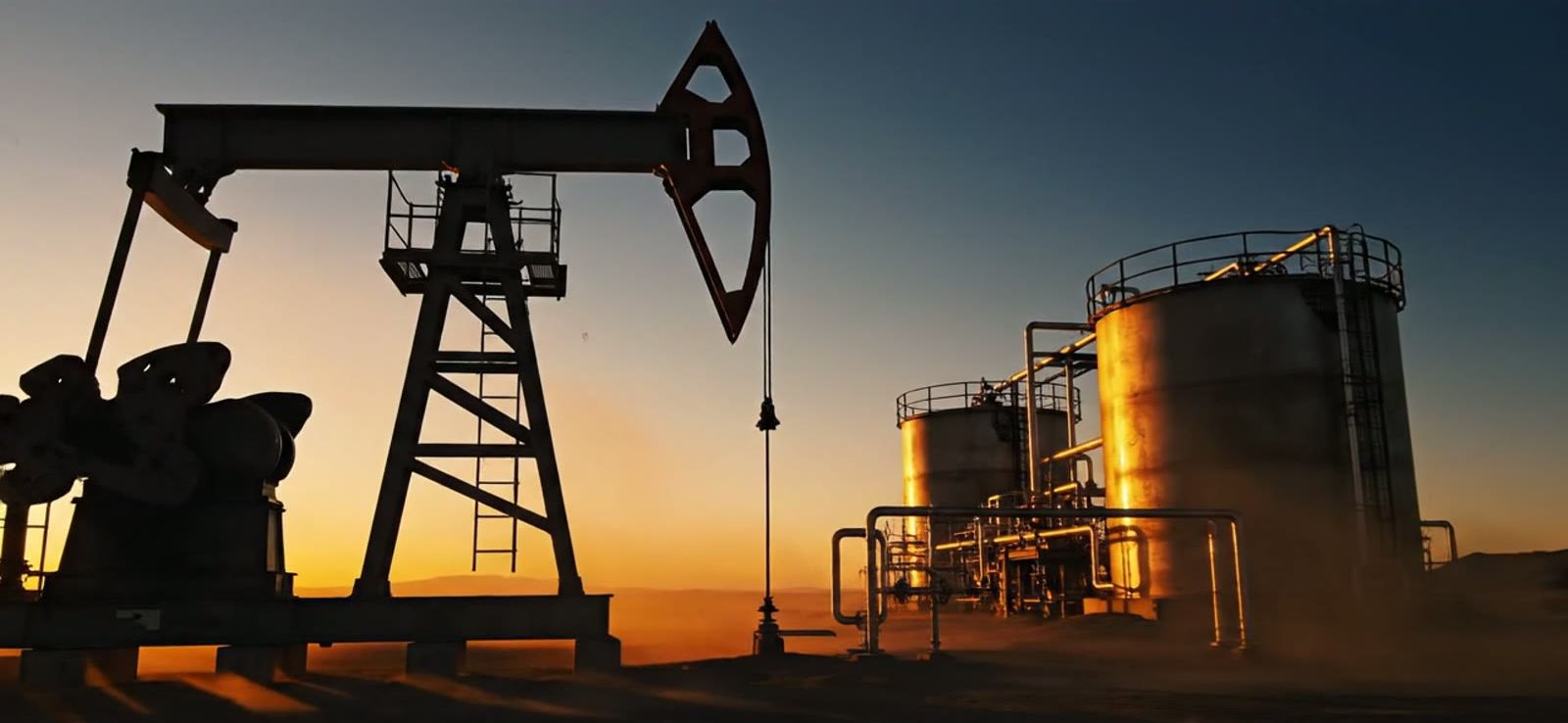 Oil pump jack and storage tanks at a remote well site at sunset