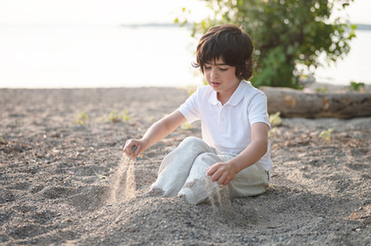 A boy in white playing in the sand on the beach