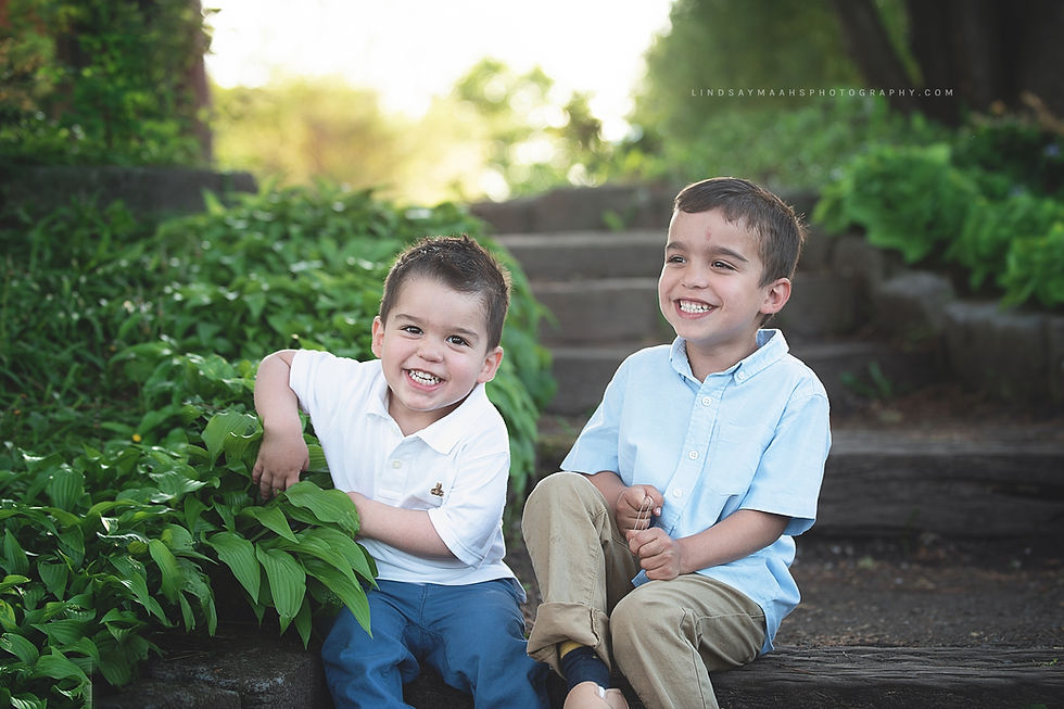 Portrait of two boy siblings together laughing sitting on stairs beside hostas