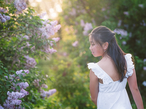 girl looking over her shoulder standing beside lilacs