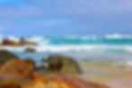 Rocky shoreline with turquoise waves crashing under a cloudy sky. The scene is vibrant and dynamic, evoking a sense of natural power at Blueys Beach NSW