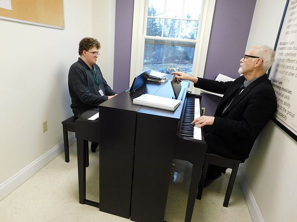 Image of Mark Palardy, seated at the left piano, and Tom Slowick, seated at the right piano, in the middle of a piano lesson in the BHMA purple studio.
