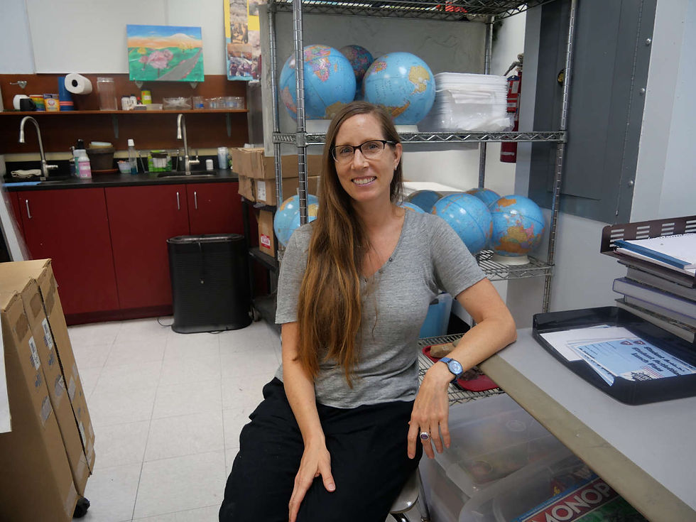 Smiling teacher sits in classroom with globes