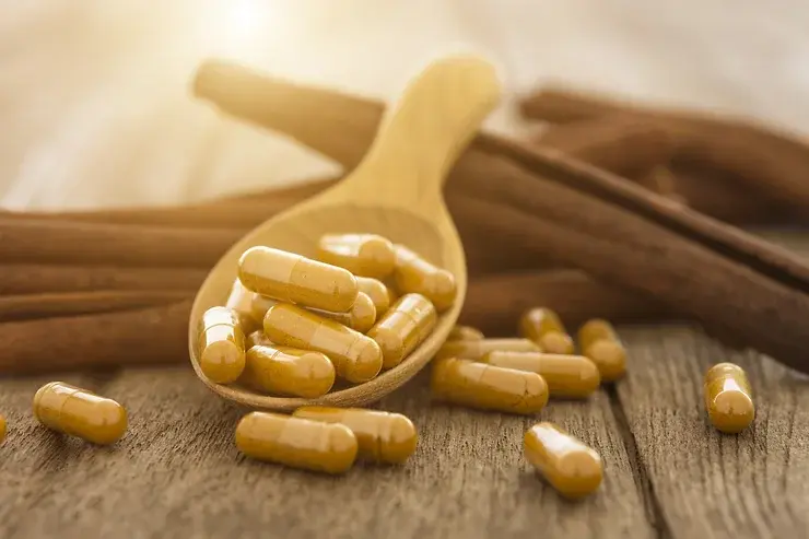 Wooden spoon holding cinnamon capsules placed on a pile of cinnamon sticks, natural ingredient setting showcasing botanical
