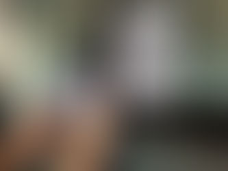 Hands holding a smartphone scanning a QR code on glass. Background shows a paper sign with QR code and "QR CODE PAYMENT" text. Bright setting.