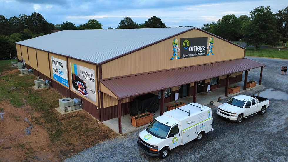 Omega printing warehouse with branded signs and two white service trucks parked outside under a cloudy sky