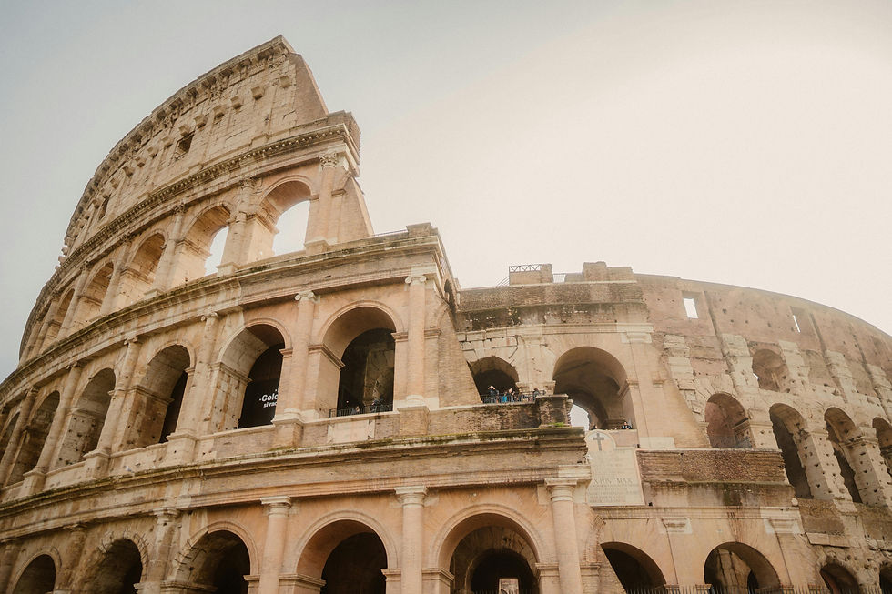 The Colosseum in Rome, displaying its ancient arches and stonework under a clear sky. Tourists are visible on the second level.