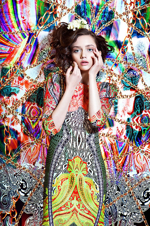 Woman in colorful dress poses in front of patterned background with flowers.