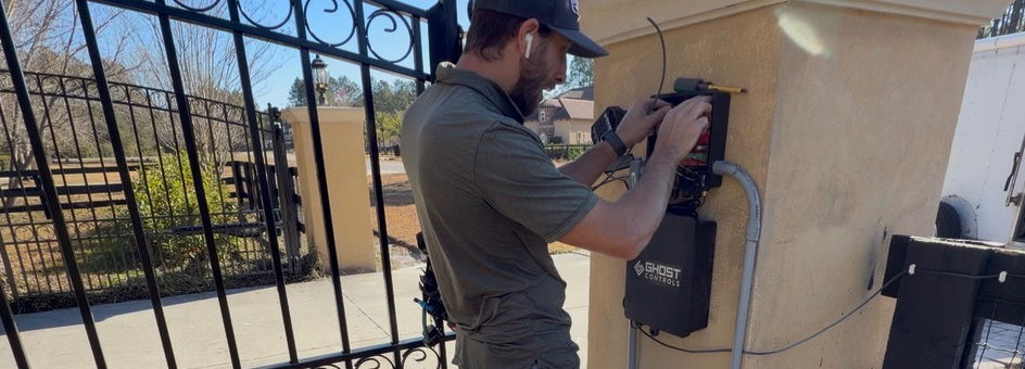 Technician installing and wiring residential swing gate control panel on masonry column