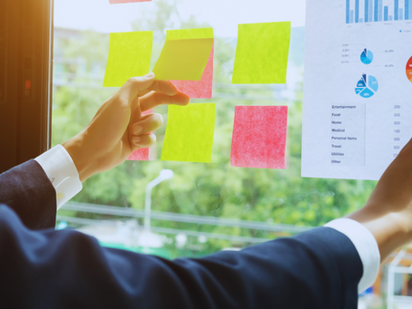 A person in business attire places colorful sticky notes on a glass wall, with charts and data visible in the background.