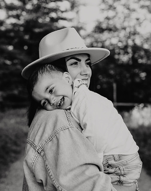 Woman in hat carries joyful child on her shoulder, outdoors black and white.