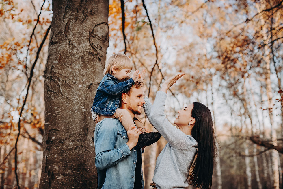 Familie mit Kind auf Schultern im bunten Herbstwald, Mutter zeigt.