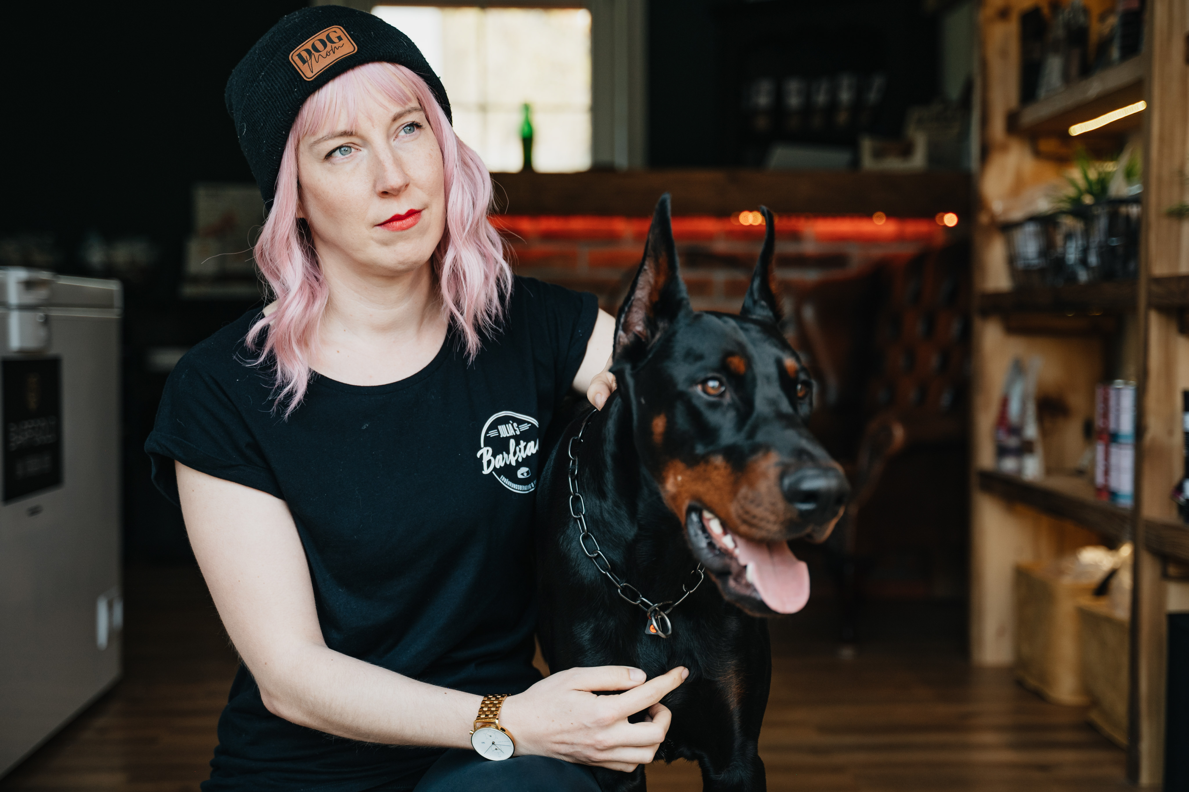 Frau mit rosa Haar, Dobermann, Beanie "DOG.", "Barklie"-Shirt in Geschäft.
