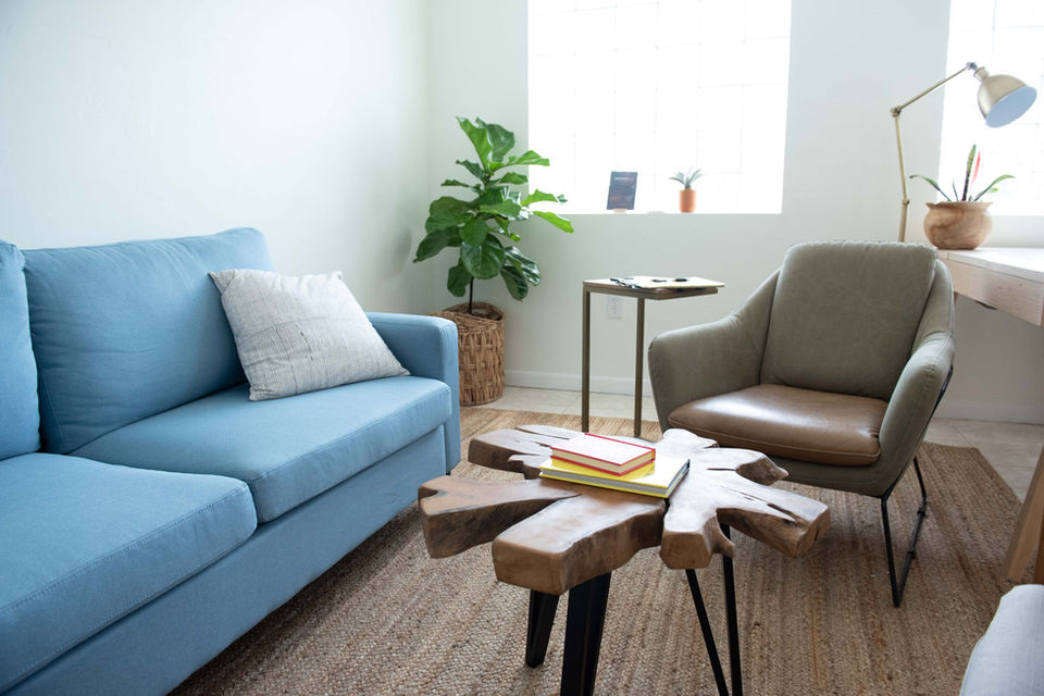 Interior photograph of a luxury penthouse living room with floor-to-ceiling windows, a modern gray sectional sofa, and a marble coffee table overlooking a city skyline.