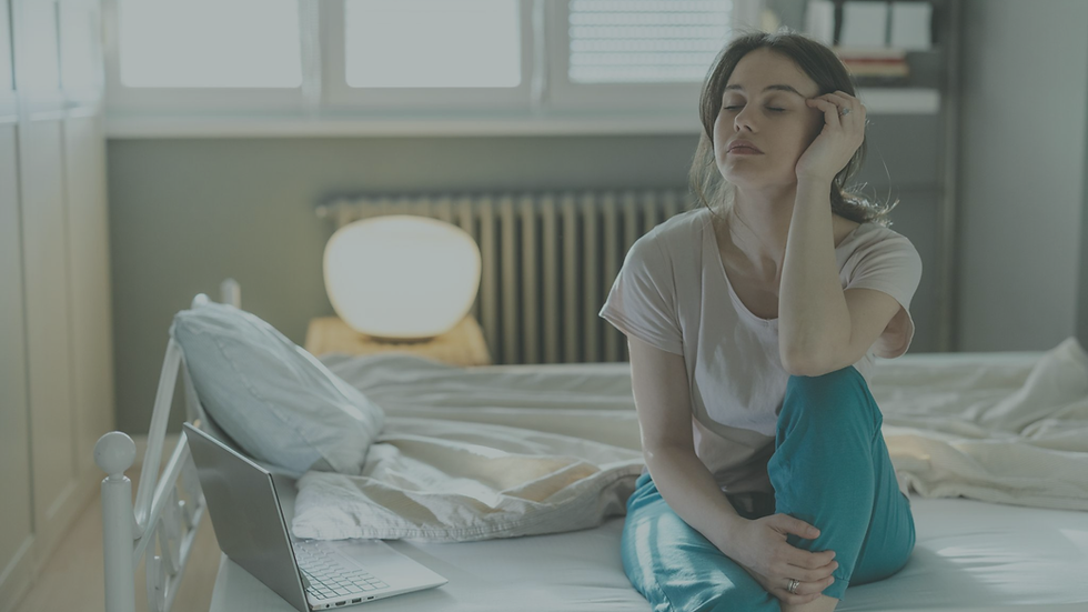 Woman sitting on the edge of her bed looking exhausted despite having slept through the night.