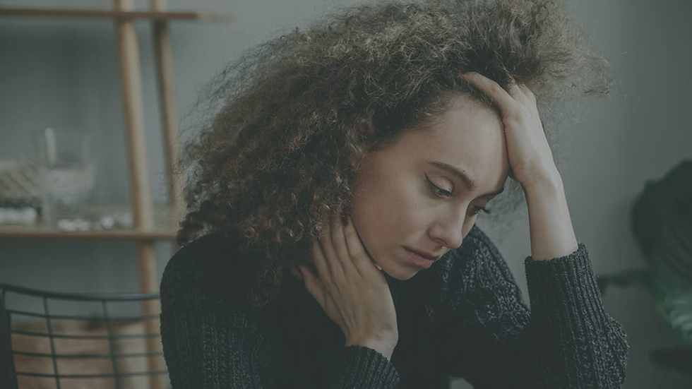 Woman sitting at home appearing emotionally overwhelmed and reflective, representing the lasting emotional effects of trauma and the journey toward healing through therapy.