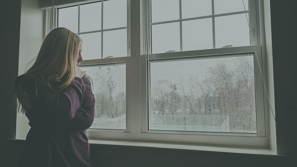 Young woman feeling loneliness looking out window on rainy day