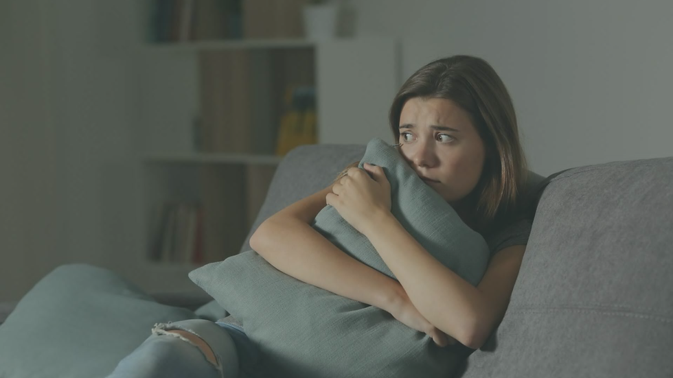 Anxious woman clutching a pillow while sitting in a quiet living room, showing how rest can feel unsafe after trauma.