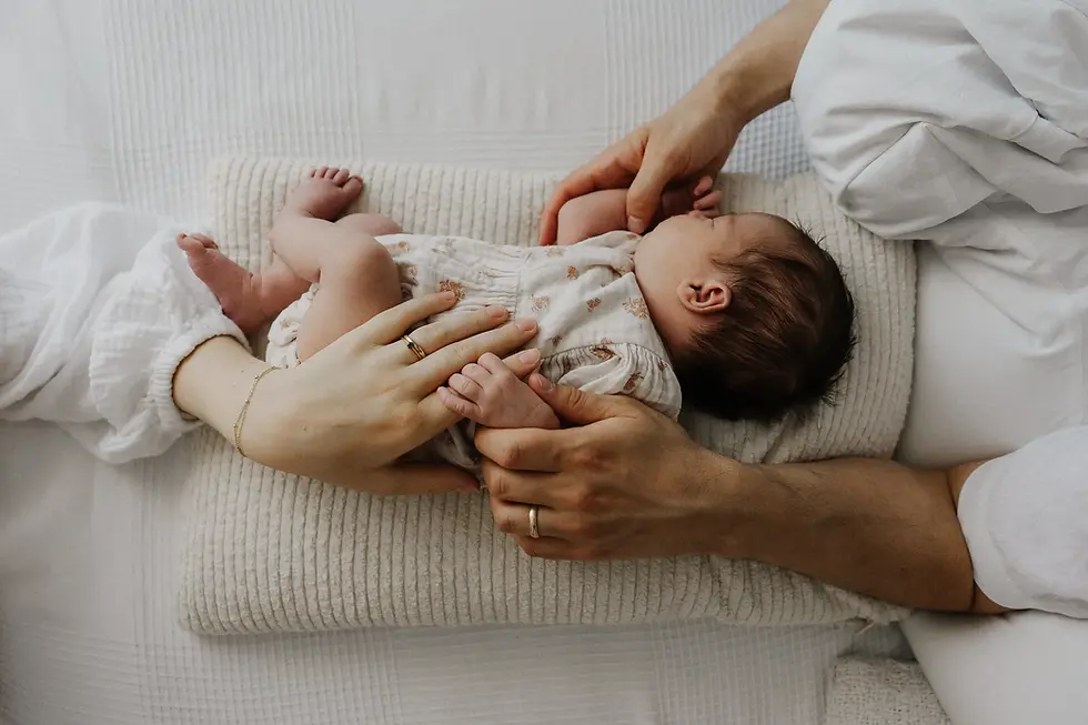 Man sieht bei diesem Nwbornshooting, wie das Baby auf einem Kissen liegt aus der Vogelperpsektive. Mama und Papa halten das Baby. Man sieht die Eheringe an den Händen.