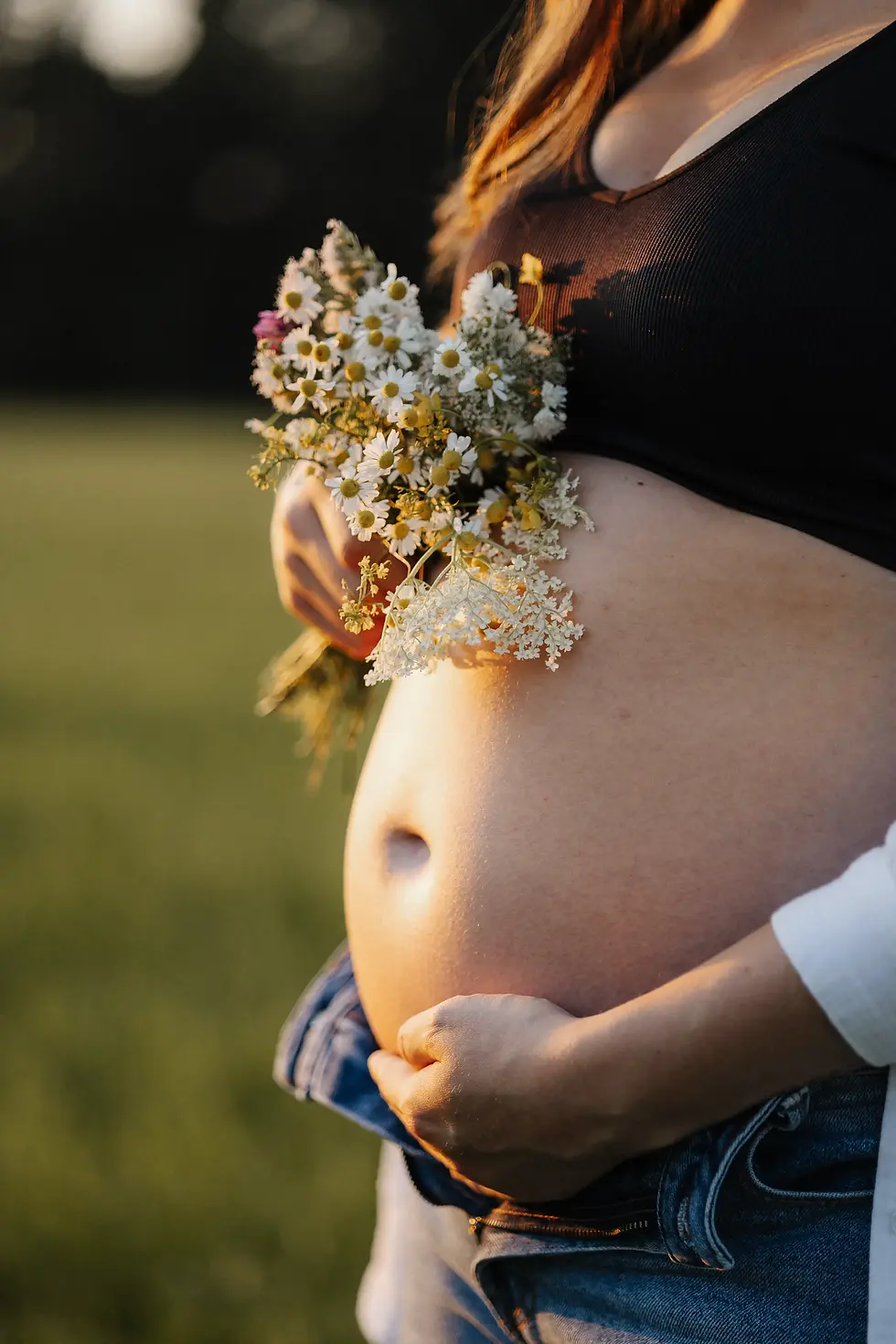 Babybauchshooting eines nackte Babybauch im Abendlicht. Sie hält über dem Bauch einen Wildblumenstrauß.