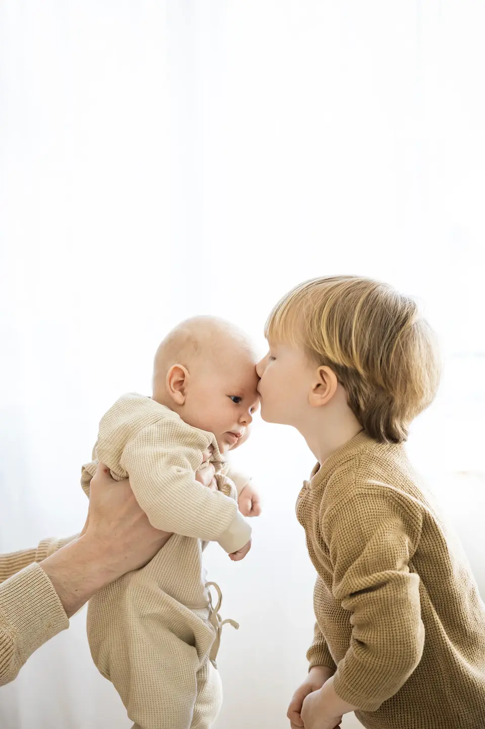 Familien Fotoshooting bei dem der Bruder seinem Neugeborenen Bruder auf die Stirn küsst.