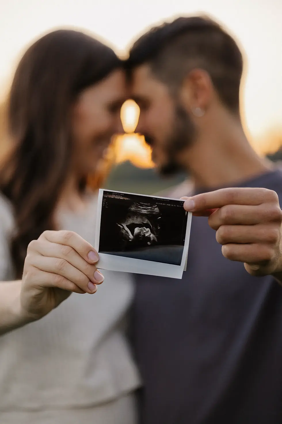 Babybauchshooting bei dem die werdenden Eltern das Ultraschallbild in den Händen halten und Stirn an Stirn sich anlehnen bei Sonnenuntergang.
